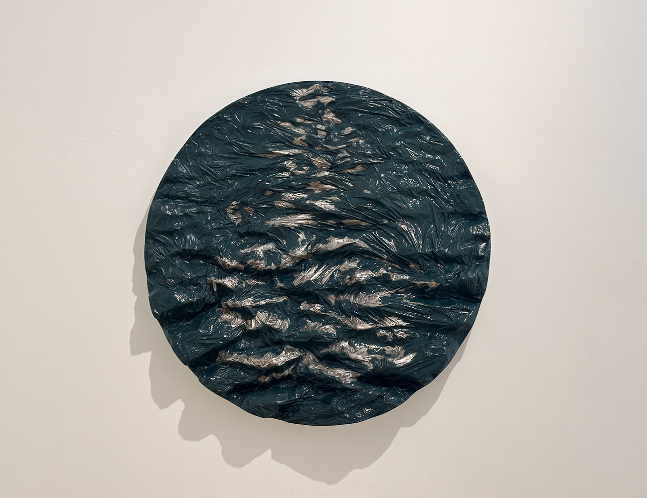 Escultura de pared en forma de tondo con superficies desiguales en un rango azulado con venas de plata que recuerda a un mar oscuro con luces frías reflejadas.